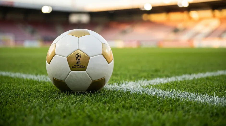 Ballon de football officiel posé sur la pelouse verte d'un stade avec les lignes blanches du terrain en arrière-plan