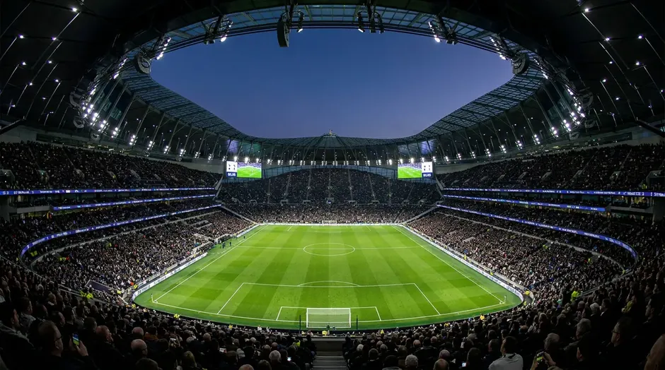 Vue panoramique d'un grand stade de football rempli de spectateurs avec la pelouse verte au centre sous les projecteurs